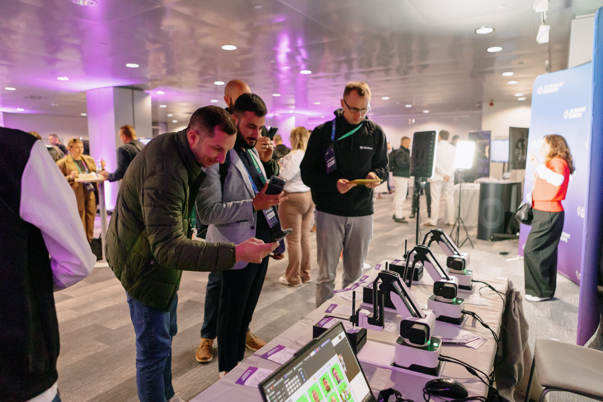 A crowd of visitors gathered around a table of robotic drawing arms at a summit